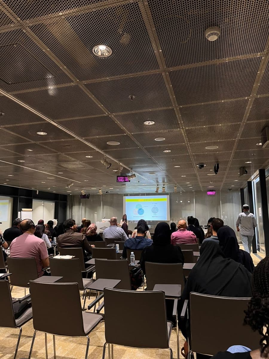 A full room of attendees watches a talk, with a slide projected at the front.