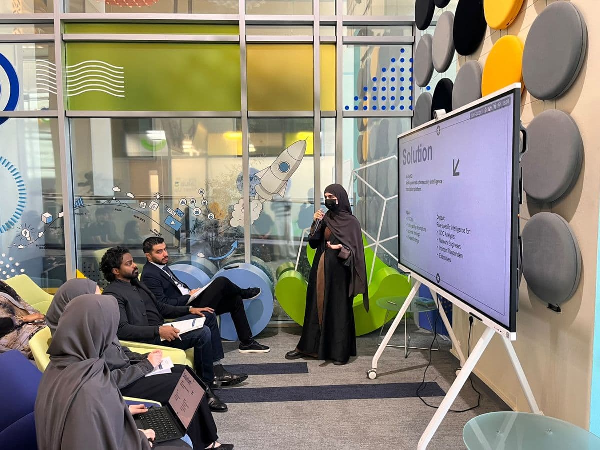 A participant presents a solution slide to a seated panel with notes and a laptop.